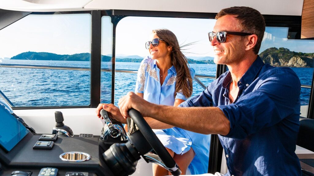 Two people in the steering station of a Jeanneau enjoying clear blue waters