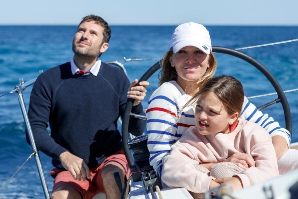 Two parents and their young child at the wheel of a Jeanneau Sun Odyssey 350