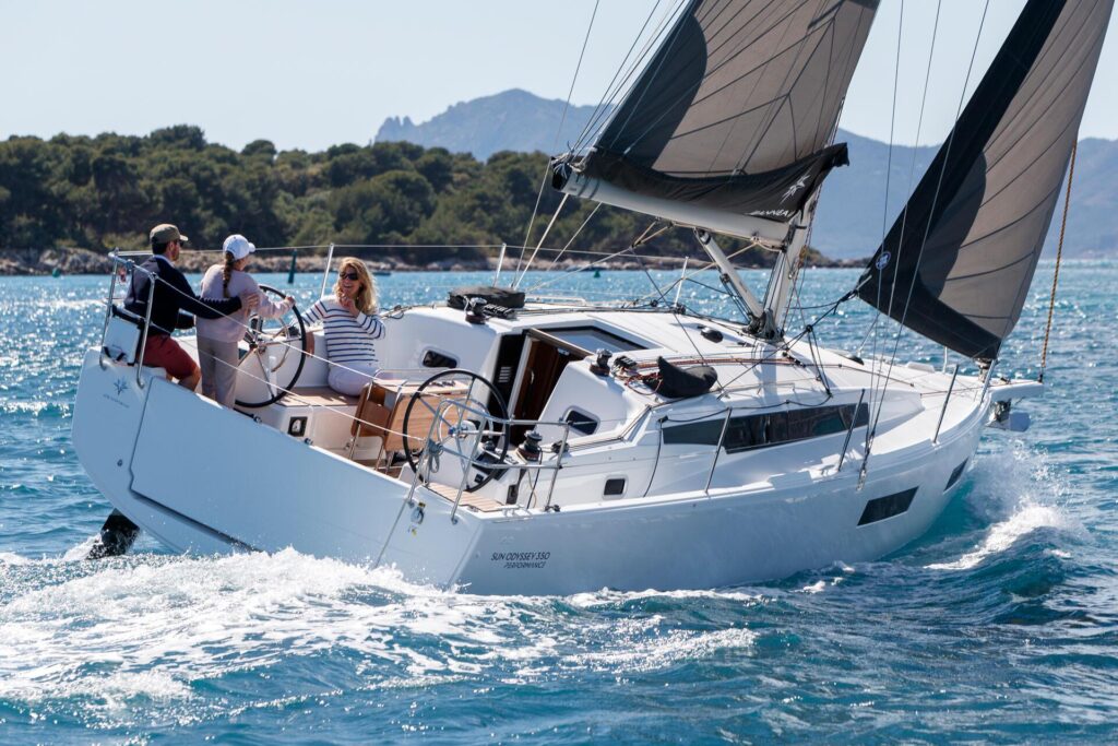 Two parents and their young child at the wheel of a Jeanneau Sun Odyssey 350. The dad is teaching the child how to steer.
