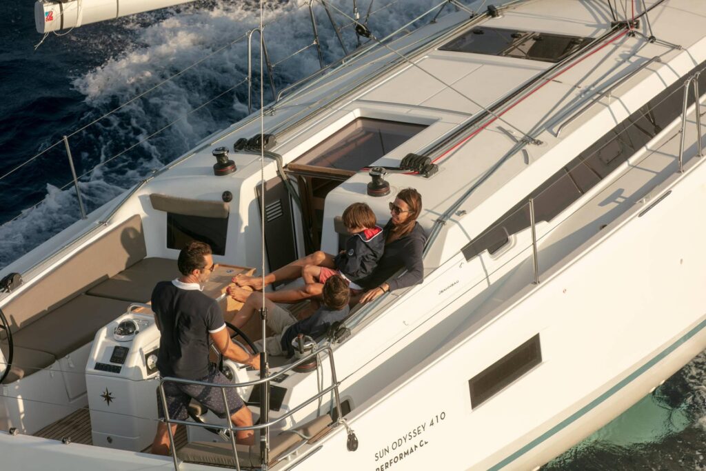 Parents and two kids relaxing on a jeanneau sun odyssey 410 while the dad steers the ship.